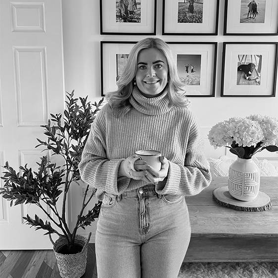 Leanne Stokes, Denvirmarketing's Senior Digital Brand Manager, holding a mug of coffee while leaning against a table, smiling at the camera